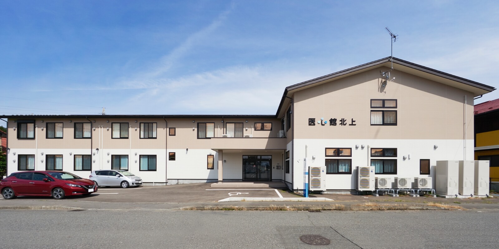 介護施設の建物外観。クリーム色の2階建て建物と駐車場が見える。